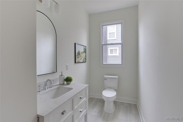 half bathroom featuring toilet, vanity, and baseboards