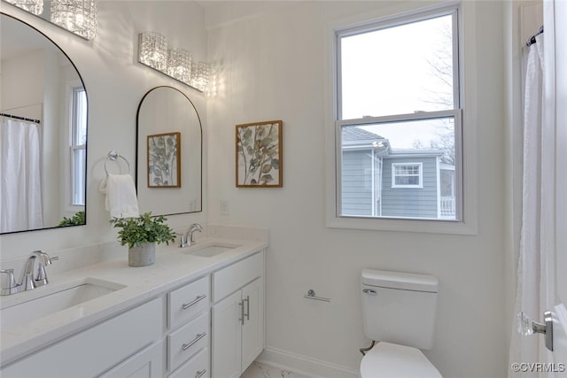 bathroom featuring double vanity, toilet, baseboards, and a sink