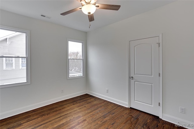 empty room featuring ceiling fan, visible vents, baseboards, and dark wood-style floors