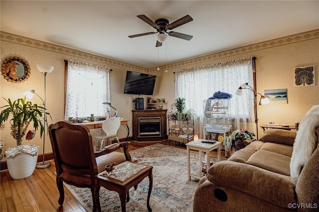 living area featuring a fireplace, baseboards, ceiling fan, and hardwood / wood-style floors