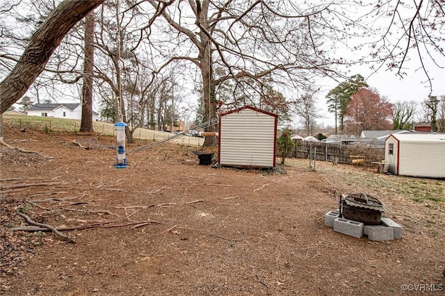 view of yard featuring an outbuilding, a fire pit, fence, and a shed