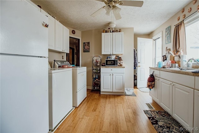 kitchen with visible vents, light wood-style flooring, washer and clothes dryer, freestanding refrigerator, and black microwave