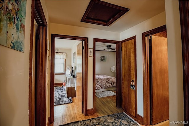 hall with baseboards, attic access, and wood finished floors