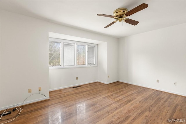 empty room featuring a ceiling fan, wood finished floors, visible vents, and baseboards