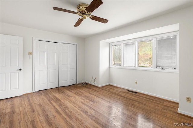 unfurnished bedroom featuring wood finished floors, visible vents, baseboards, ceiling fan, and a closet