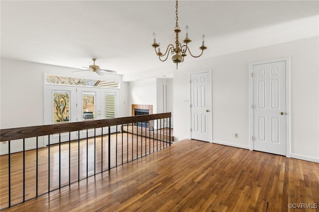 interior space with baseboards, wood finished floors, a tiled fireplace, and ceiling fan with notable chandelier