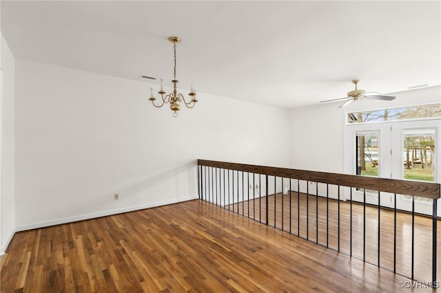 empty room with visible vents, ceiling fan with notable chandelier, baseboards, and wood finished floors