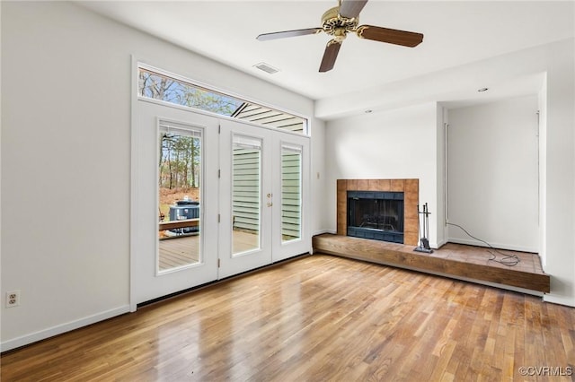 unfurnished living room with a tiled fireplace, wood finished floors, visible vents, and baseboards