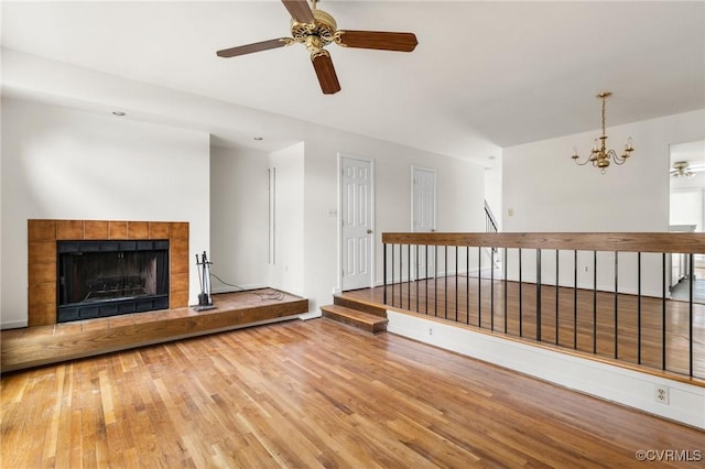 unfurnished living room with baseboards, wood finished floors, a fireplace, and ceiling fan with notable chandelier