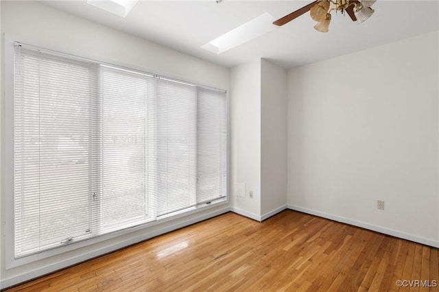 unfurnished room featuring light wood-style flooring, a skylight, a ceiling fan, and baseboards