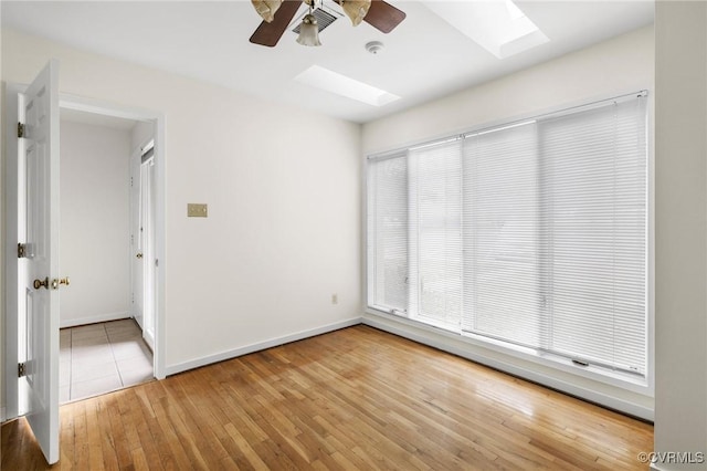 unfurnished room featuring baseboards, a skylight, light wood-style floors, and a ceiling fan