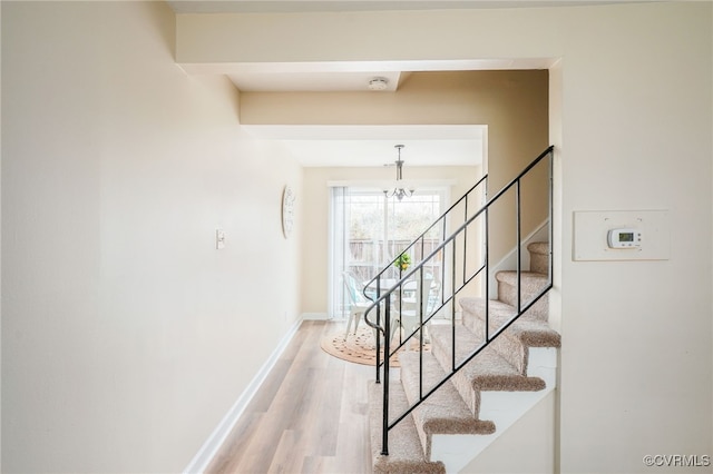 staircase featuring a notable chandelier, baseboards, and wood finished floors