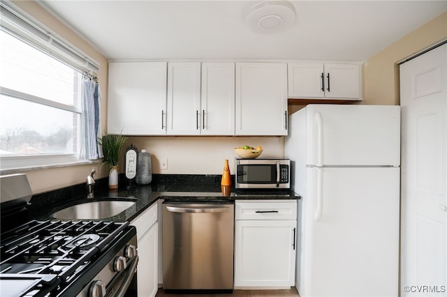 kitchen with dark stone countertops, white cabinetry, stainless steel appliances, and a sink