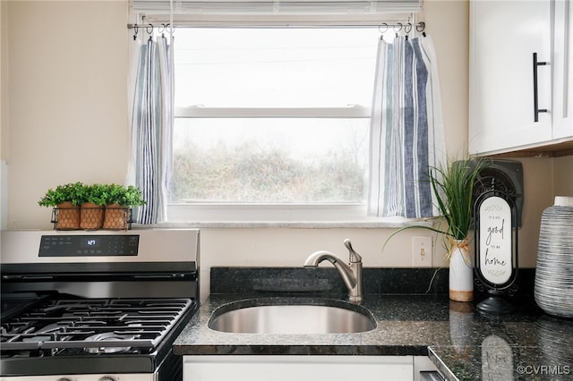 kitchen featuring dark stone countertops, white cabinets, stainless steel gas range, and a sink