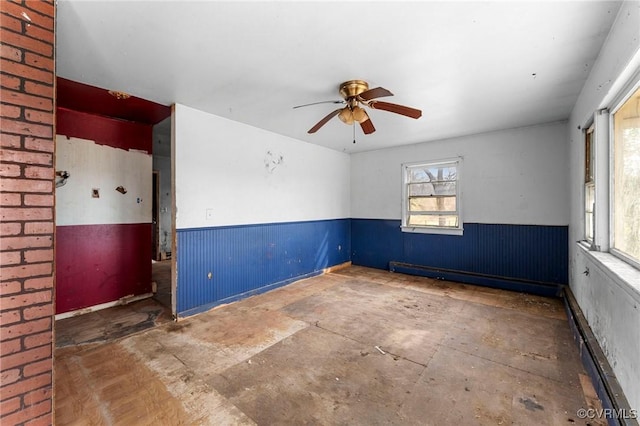 unfurnished room featuring a wainscoted wall, a baseboard heating unit, and a ceiling fan