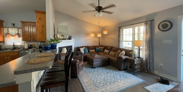 living area with vaulted ceiling, light wood finished floors, a wealth of natural light, and ceiling fan