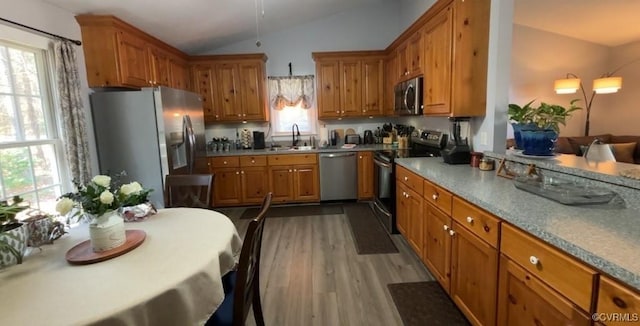 kitchen featuring a sink, wood finished floors, stainless steel appliances, brown cabinetry, and lofted ceiling