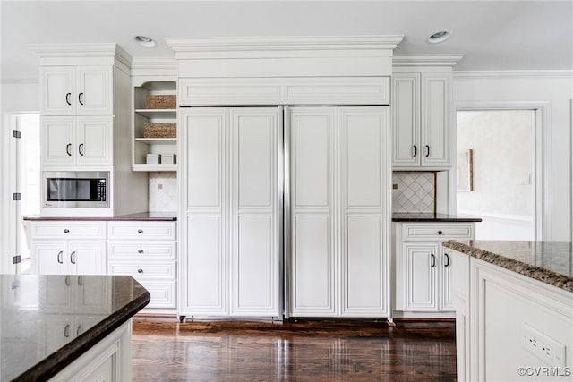 kitchen with white cabinetry, dark stone counters, built in appliances, and ornamental molding