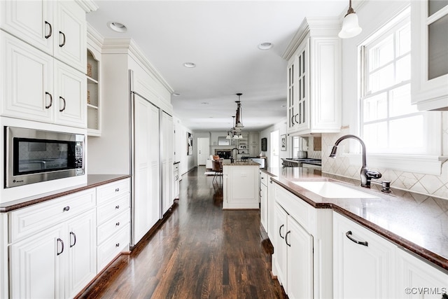 kitchen with dark wood-style floors, a sink, hanging light fixtures, stainless steel microwave, and open floor plan