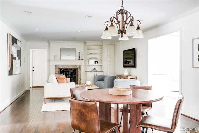 dining area featuring wood-type flooring, a notable chandelier, a fireplace, and crown molding