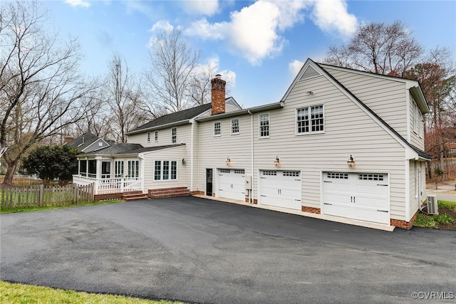 rear view of house with a garage, a chimney, driveway, and fence