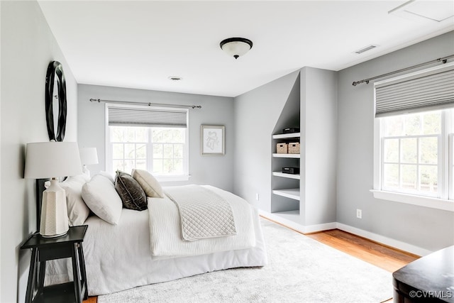 bedroom with visible vents, multiple windows, baseboards, and wood finished floors