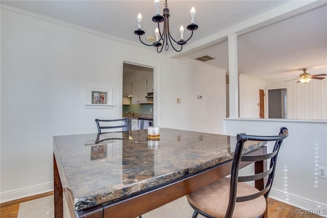 dining room featuring visible vents, ornamental molding, ceiling fan with notable chandelier, light wood-style floors, and baseboards