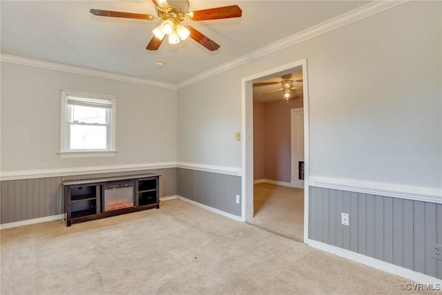 unfurnished room featuring carpet flooring, wainscoting, a ceiling fan, and ornamental molding