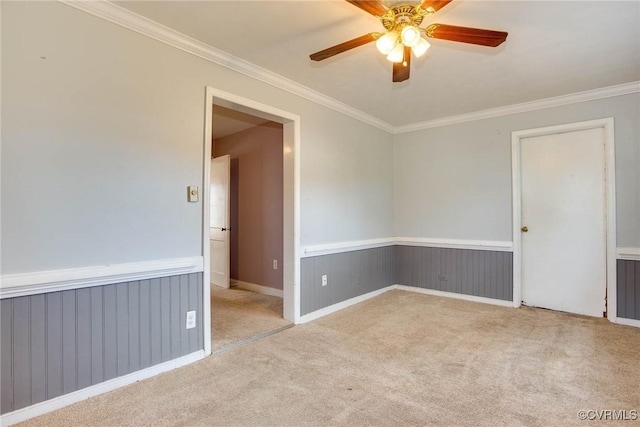 spare room featuring wainscoting, carpet floors, ornamental molding, and a ceiling fan