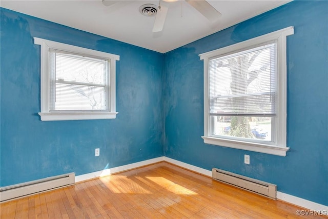 empty room featuring a baseboard heating unit, wood-type flooring, baseboard heating, and visible vents