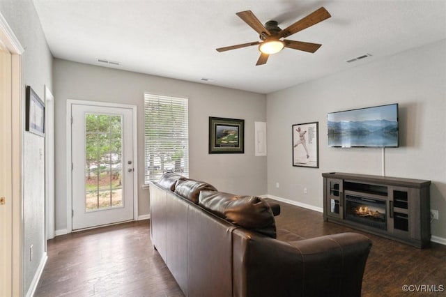 living room featuring visible vents, baseboards, dark wood-type flooring, and ceiling fan