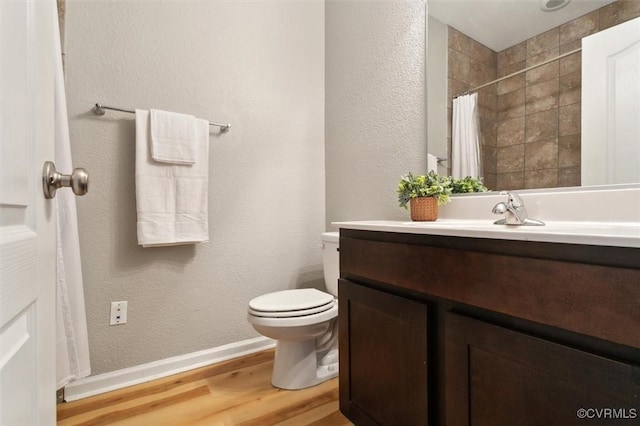 bathroom featuring vanity, wood finished floors, baseboards, a tile shower, and toilet