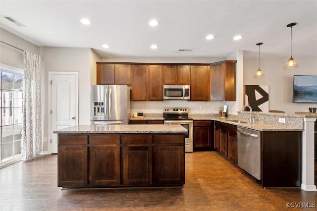 kitchen featuring light stone countertops, a kitchen island, dark wood-style flooring, a sink, and stainless steel appliances