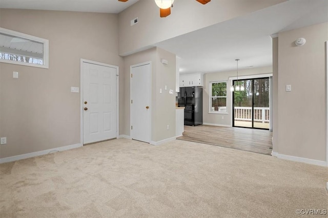 entrance foyer featuring visible vents, high vaulted ceiling, a ceiling fan, baseboards, and light colored carpet