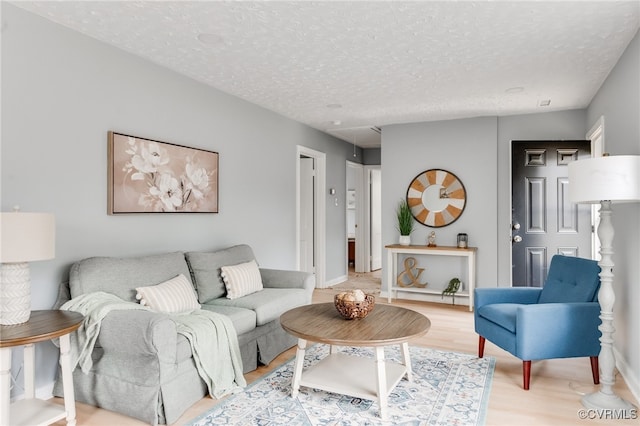 living room featuring baseboards, light wood-type flooring, and a textured ceiling