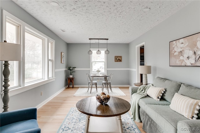 living area with baseboards, a textured ceiling, and light wood finished floors