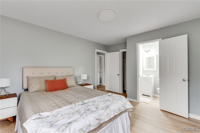 bedroom featuring connected bathroom, baseboards, and light wood finished floors