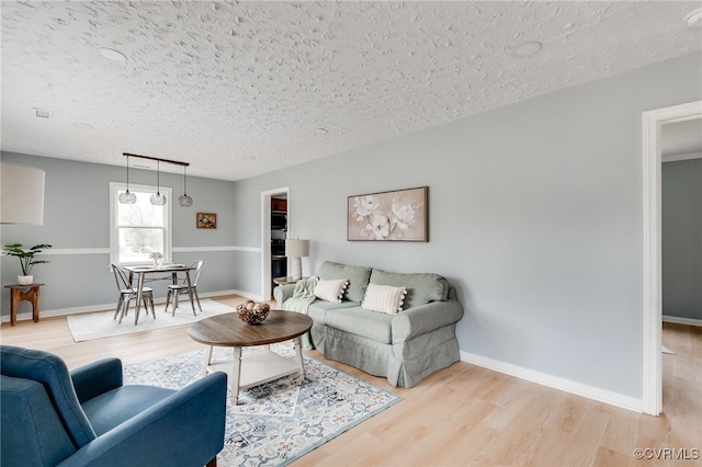 living room featuring baseboards, a textured ceiling, and light wood-style floors