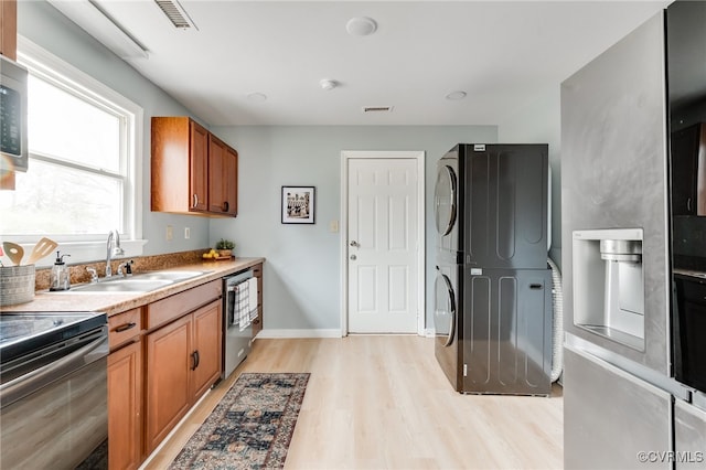 kitchen featuring visible vents, brown cabinets, stainless steel appliances, stacked washer / drying machine, and a sink