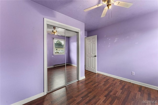 unfurnished bedroom featuring a ceiling fan, wood finished floors, a closet, a baseboard radiator, and baseboards