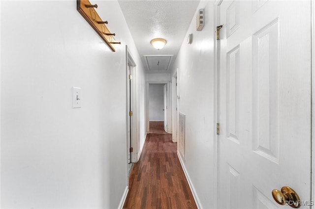 hallway featuring baseboards, a textured ceiling, attic access, and dark wood-style floors