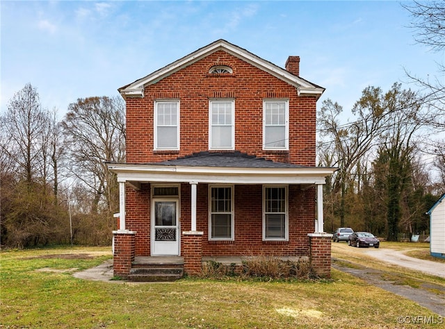 view of front of property with driveway, a front lawn, covered porch, brick siding, and a chimney