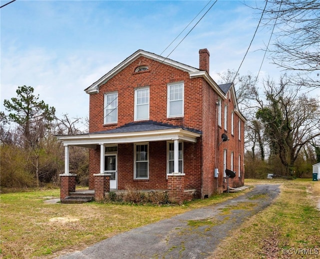 view of front of house with brick siding, a front lawn, covered porch, a chimney, and driveway