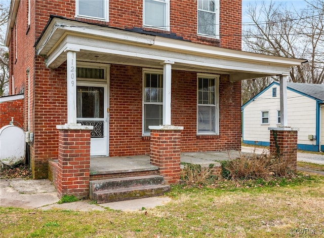 view of exterior entry with brick siding, covered porch, and heating fuel