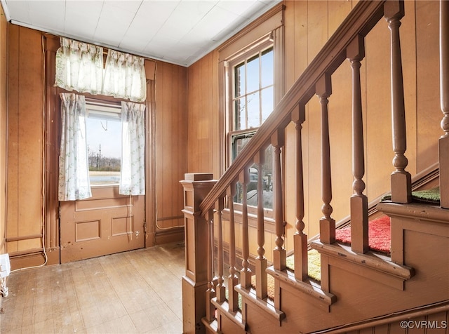 foyer entrance with light wood-type flooring, stairway, and wooden walls