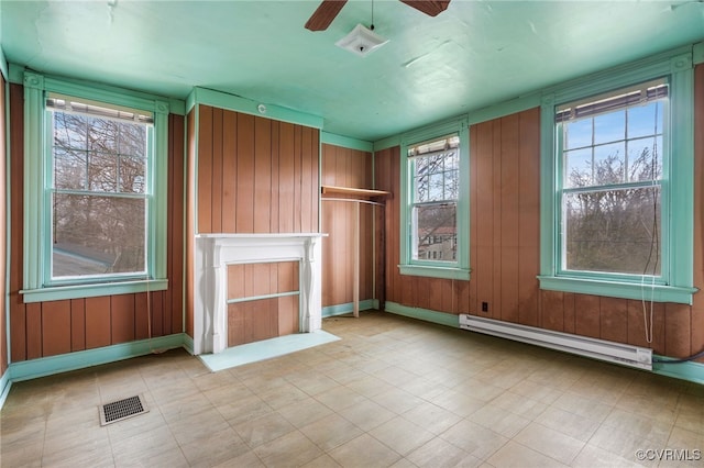 unfurnished living room with a baseboard heating unit, plenty of natural light, a ceiling fan, and visible vents