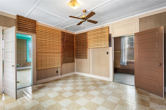 spare room featuring baseboards, ceiling fan, light floors, wood walls, and baseboard heating