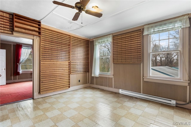 empty room with a baseboard heating unit, tile patterned floors, a ceiling fan, and wood walls