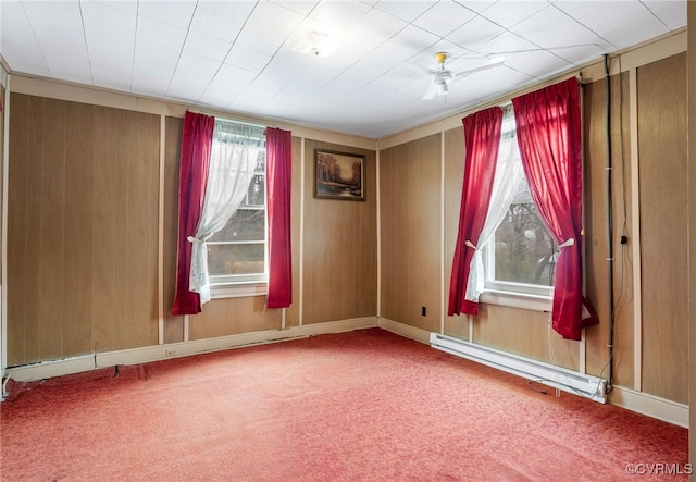 carpeted spare room with baseboard heating, wood walls, and a ceiling fan