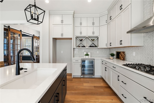 kitchen with wall chimney range hood, wine cooler, light countertops, light wood-style flooring, and a sink